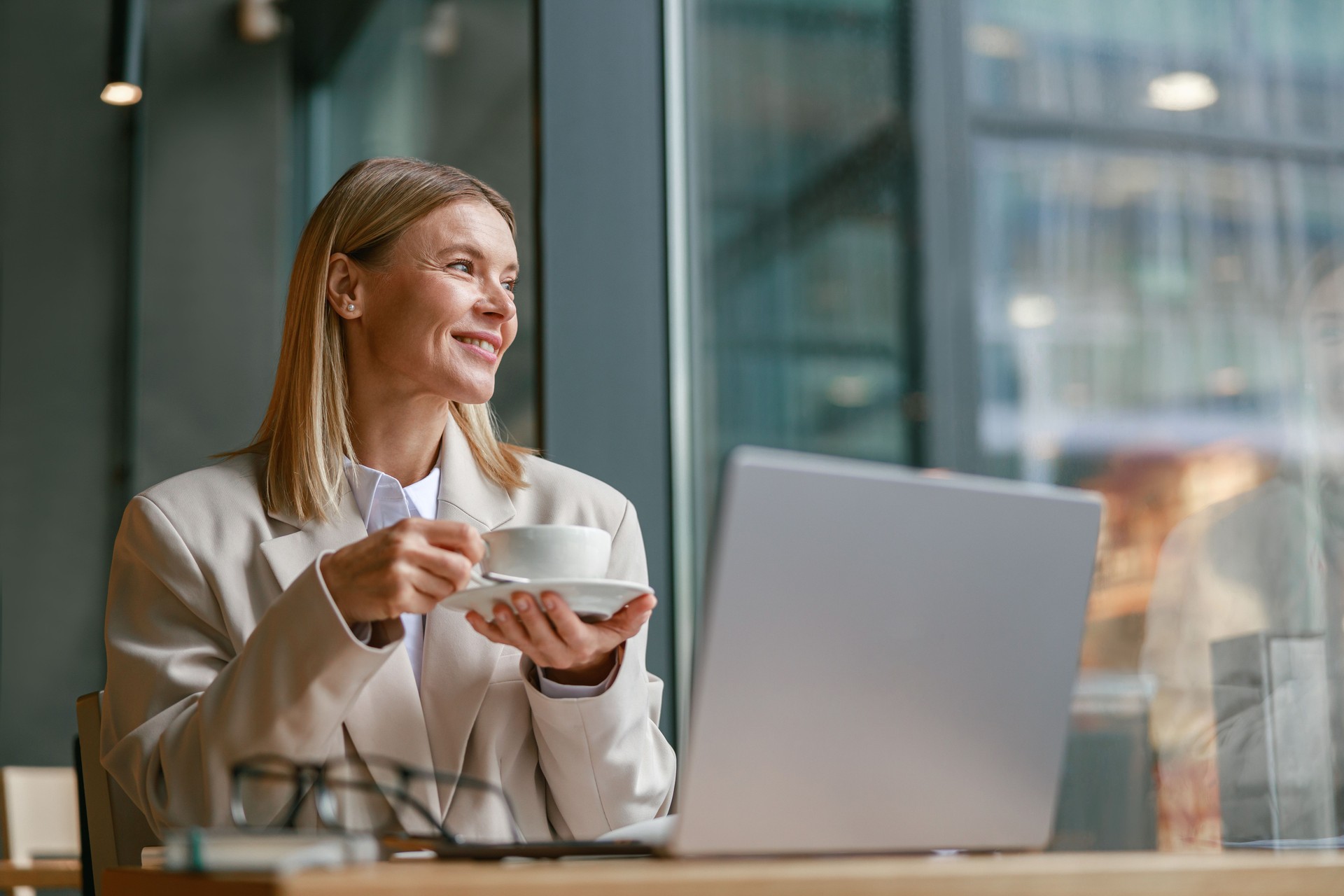 Smiling businesswoman having coffee break time during working day in cafe and looking at window